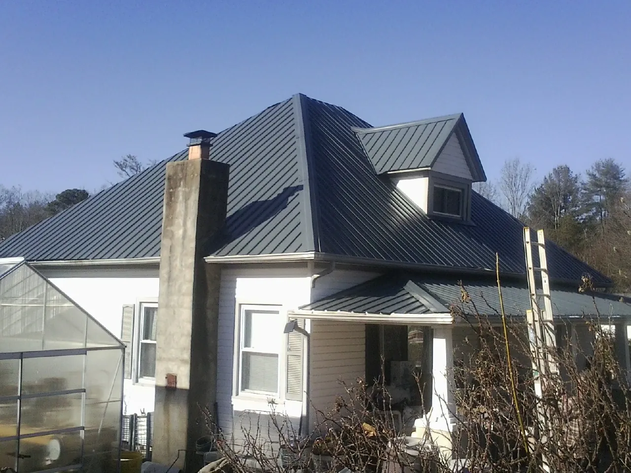 Dark blue standing seam metal roof on a white farmhouse with dormer — Slate & Tile Roof Repair by Roofing Brothers in Lingle
