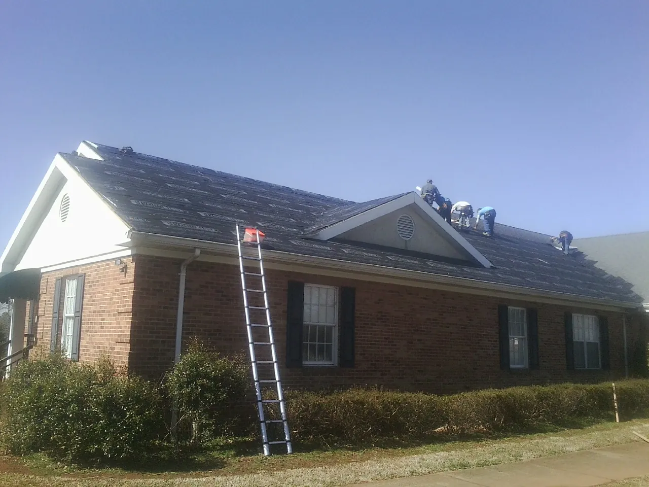 Crew tearing shingles off a brick ranch roof with a ladder set — Emergency Roof Repair work by our crew in Lingle