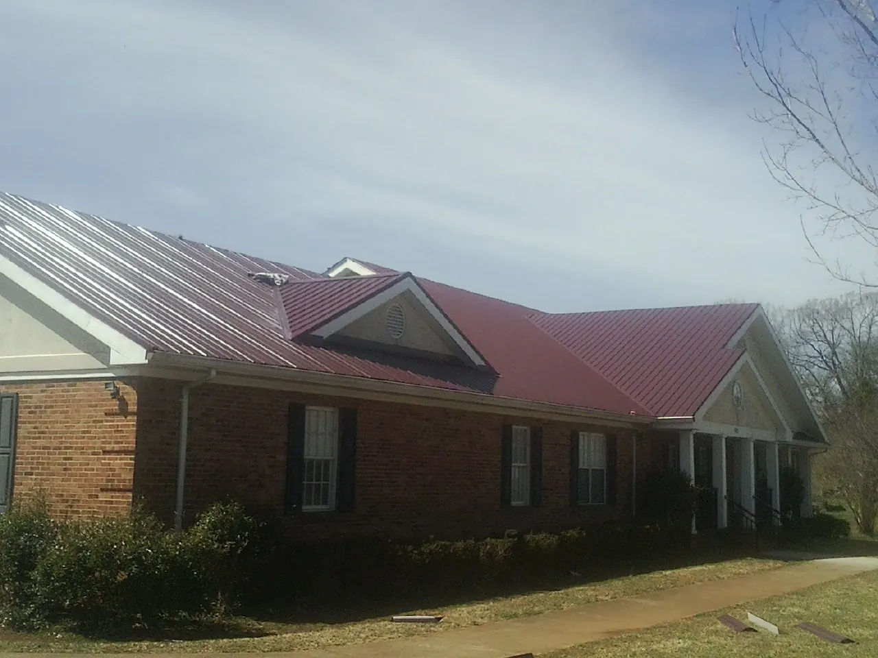 Red metal roof with gabled entries on a long brick building, from a Hail Damage Roof Repair job in Lingle
