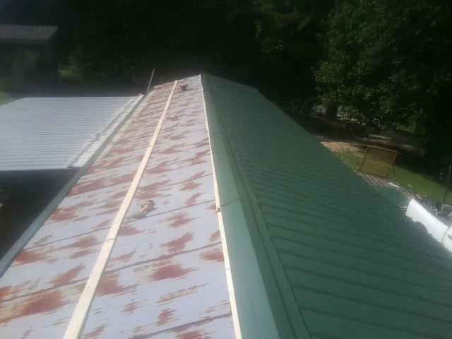 Old rusted panels beside newly installed green metal roofing — Wind Damage Roof Repair by Roofing Brothers in Lingle