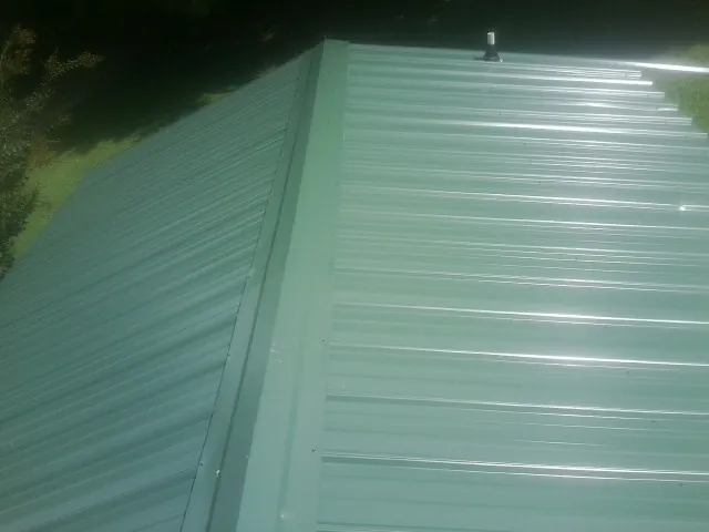 New green metal panels meeting at the ridge of a roof — Flat Roof Repair work by our crew in Lingle