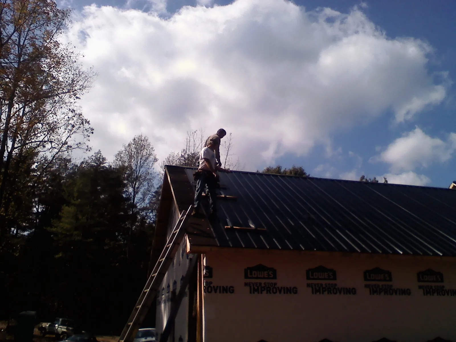 Roofer fastening dark metal panels high against a cloudy sky, from a Roof Inspection job in Lingle