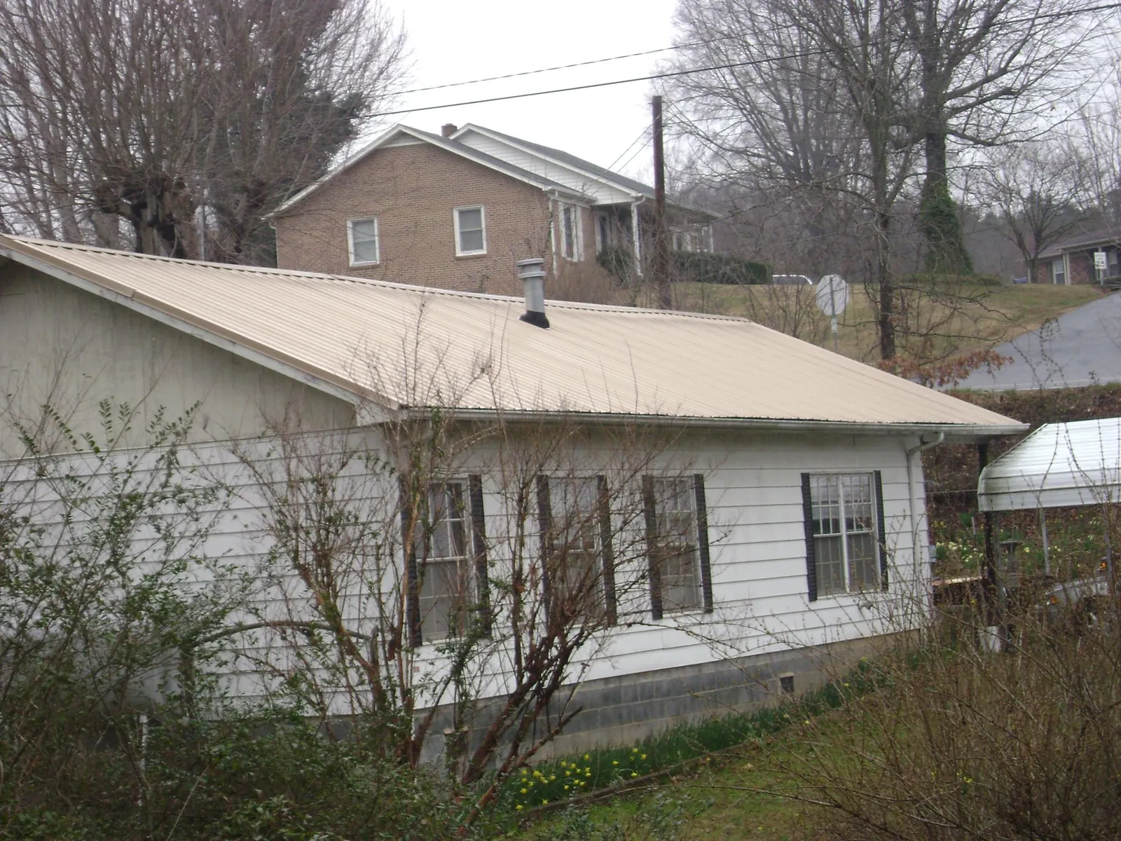 Tan metal roof on a white sided house set into a hillside — Commercial Roofing by Roofing Brothers in Lingle
